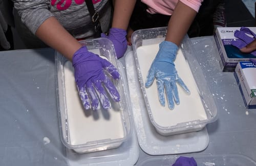 Two hands in latex gloves pressing into tubs of plaster