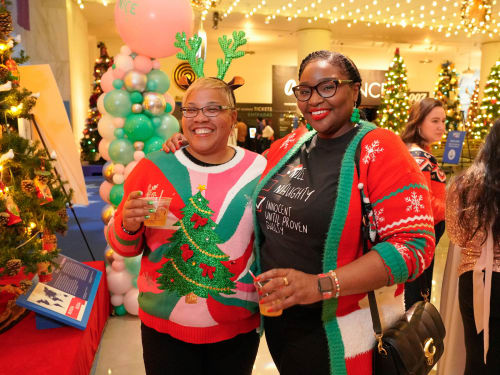 Two friends in holiday sweaters and antlers posing with adult beverages
