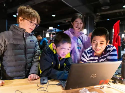 Campers smiling and gathered around laptop