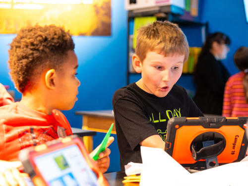 Camper talks animatedly to another while looking at tablet