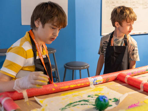 Two campers in aprons at tables working with paint