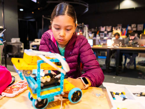 Camper at a lab table works on a wheeled robot vehicle