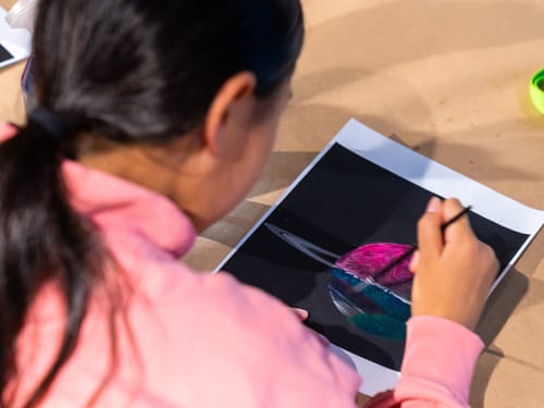 View over shoulder of camper painting a picture of a planet 