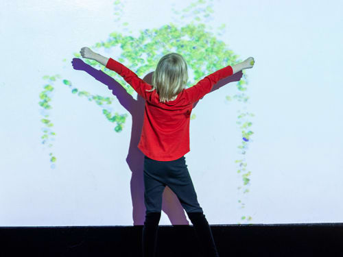 Young child with arms spread interacting with a projection of falling beads