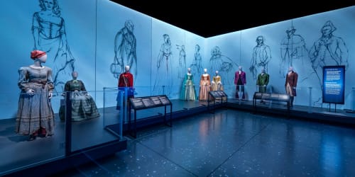 A wide shot of a gallery in "Crafting Character: The Costumes of Paul Tazewell" featuring costumes from 'Hamilton' and 'Harriet'.