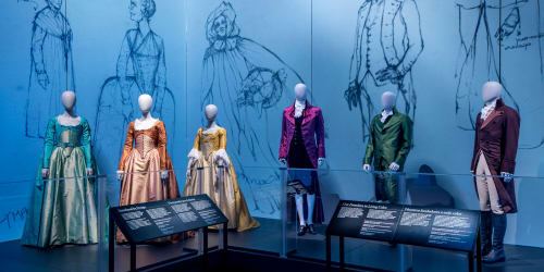 Colorful dresses and suits from the hit-musical 'Hamilton' on display. Preliminary sketches of the costumes are displayed on the wall behind.