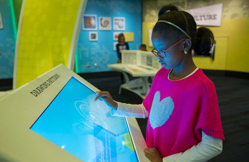 Girl in pink shirt feature a white heart touches a “Drawing Patterns” interactive screen