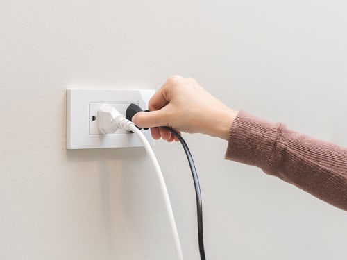 Wall power outlet with a hand plugging in a cord