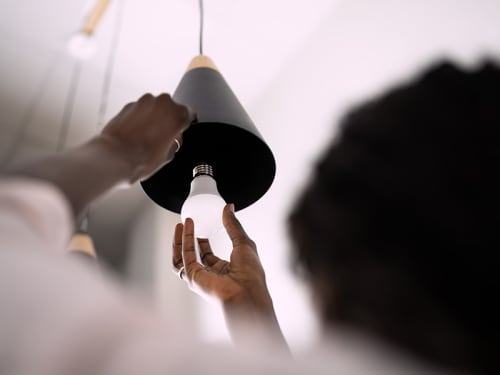 Person replacing hanging lamp's bulb with an LED bulb
