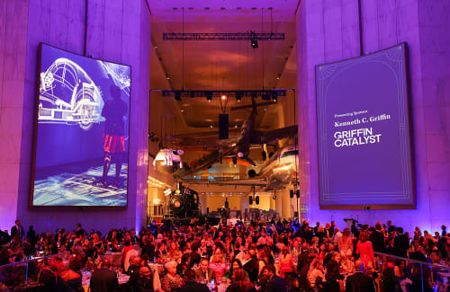 Seated dinner crowd in the Museum Rotunda below two large digital event signs