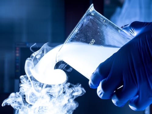 Gloved hand pouring a beaker of liquid nitrogen vapor