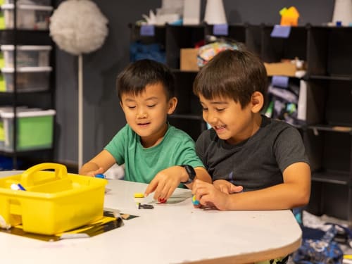 Two young campers are all smiles collaborating on a craft.