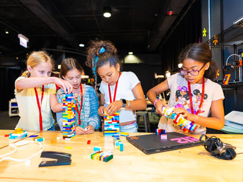 Four girls wearing lanyards assembling LEGO® structures at a table