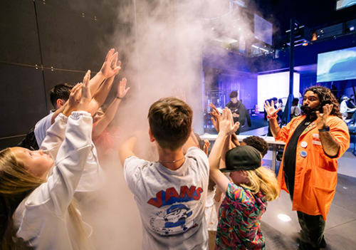 Museum facilitator talking to guests standing with hands up in an air vortex 