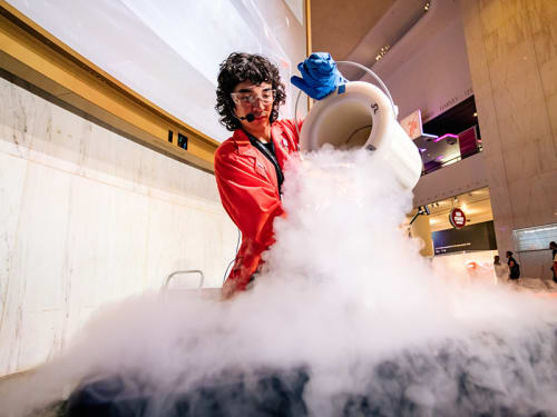 Museum facilitator in goggles and gloves pouring a container releasing vapor clouds