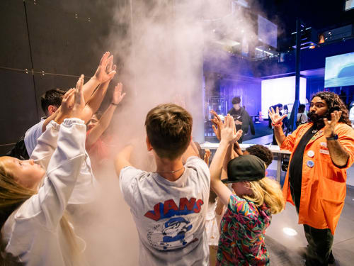 Museum facilitator talking to guests standing with hands up in an air vortex 