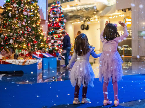 Two children playing below falling indoor "snow" in the Museum's holiday exhibit