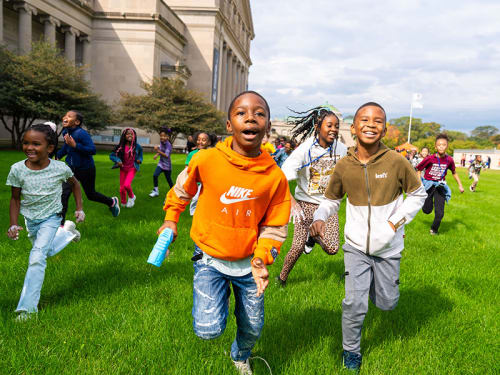 Excited young children running toward the camera on the Museum front lawn