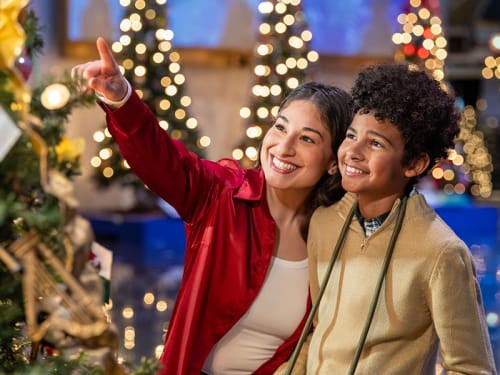 Woman (who points) and young teen smiling among a display of holiday trees
