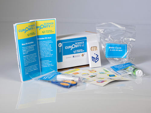 The contents of the "Blue" Science Curiosity Kit are displayed featuring activities like The Water Cycle, Acidic, Basic or Neutral, Waste Audit, 3Rs (Reduce, Reuse, Recycle), and Advocacy.