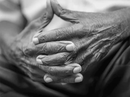 The hands of an older individual in black and white, conveying feeling of tension and uncertainty.