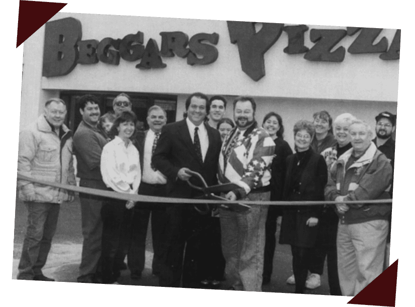 A black and white photograph of members of the Beggars Pizza team, cutting the ribbon at a franchise opening ceremony.