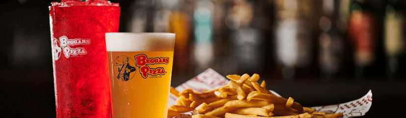 A frothy glass of beer and soft drink sit next to a basket of fries