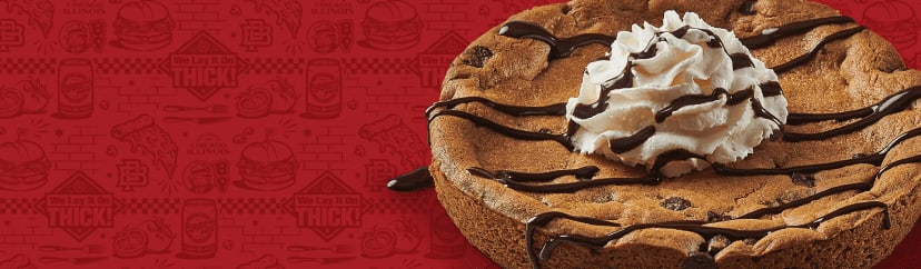 A deep-dish cookie topped with a dollop of whipped cream and a drizzle of chocolate sauce.