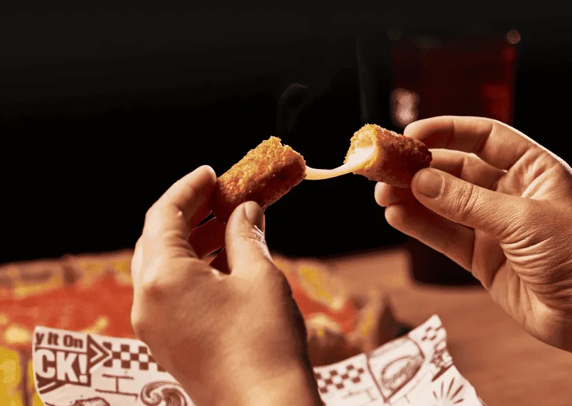 A pair of hands pull apart a mozzarella stick, with the cheese pulling from both ends.