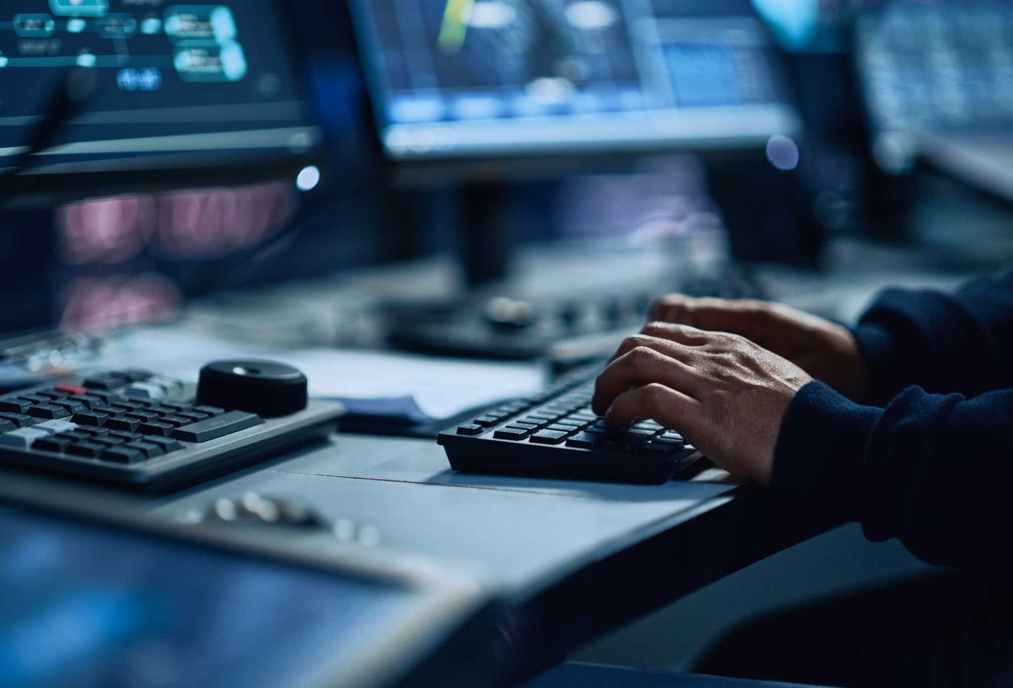 hands typing on keyboard on desk with multiple computer monitors