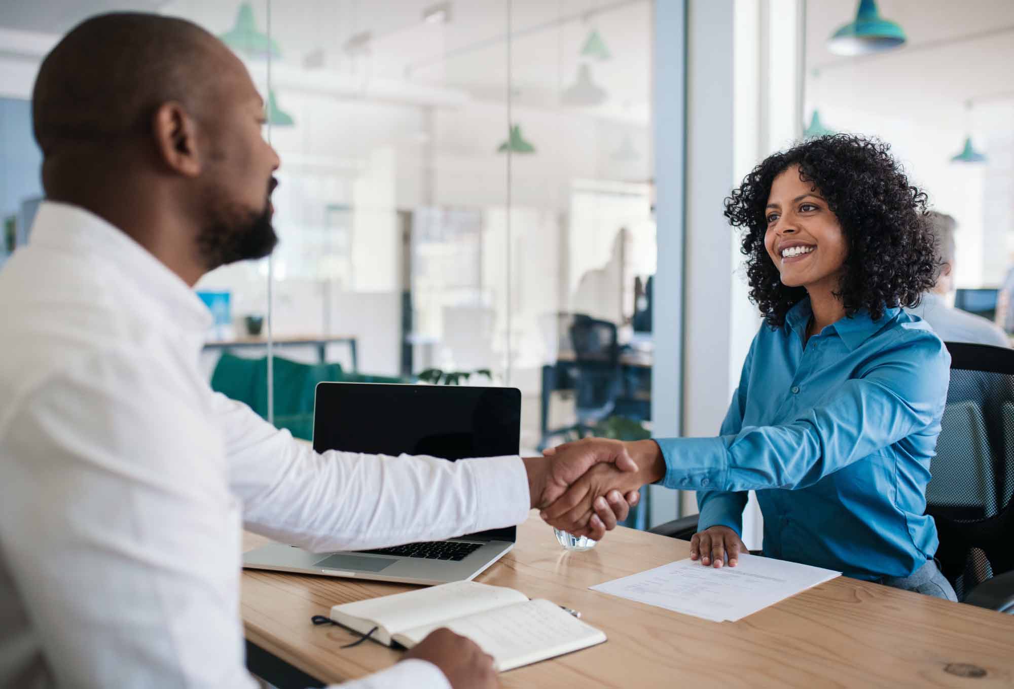 Two people shaking hands while sitting at a desk