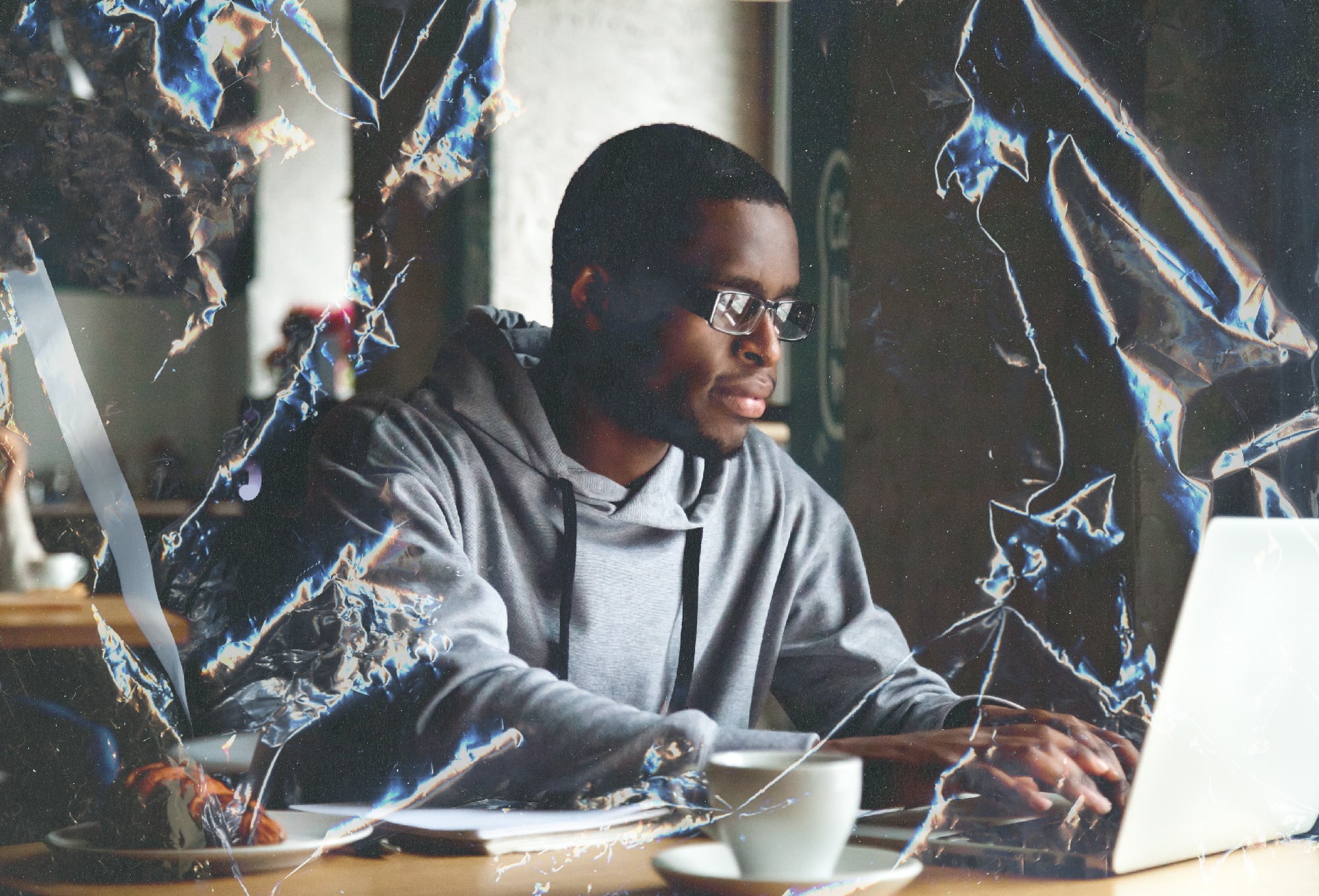 man in hoodie with glasses looking at a laptop screen with a crumpled paper photo effect overlayed