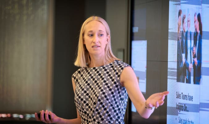 women presenting to a group pointing at a large screen