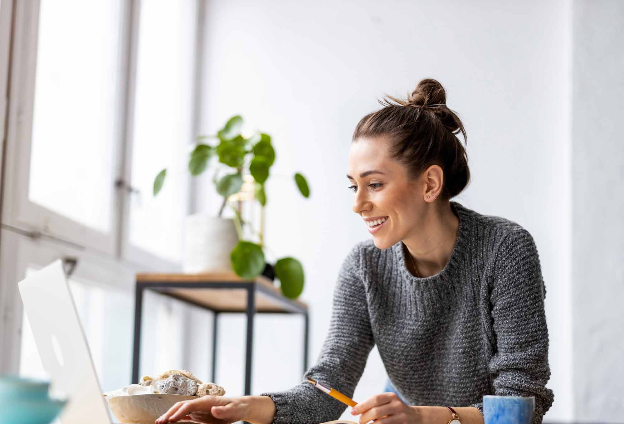 woman sitting looking over a laptop holding a pencil