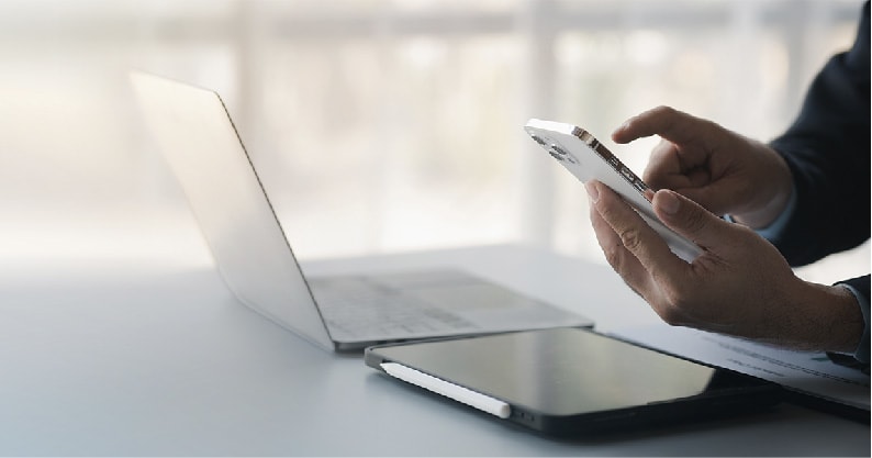 person with a laptop and ipad in a table, using their iphone