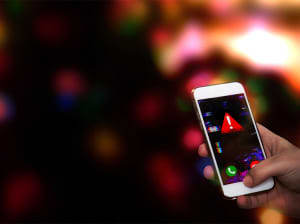 A hand holding a smartphone with a red alert symbol on it