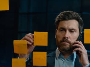 Bearded man taking a phone call working with post-its on a glass wall