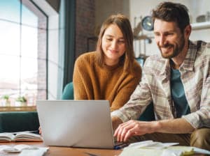Smiling man and woman sitting in a cozy nook in front of a laptop.