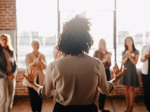 woman speaking to group of people in brick building near windows