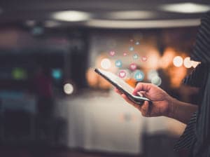 Person pressing phone screen with their hand as hearts and thumbs up bubbles float up from phone.