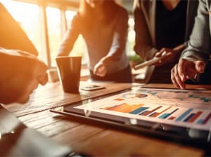 Several people gathered around a work table with a tablet displaying graphs