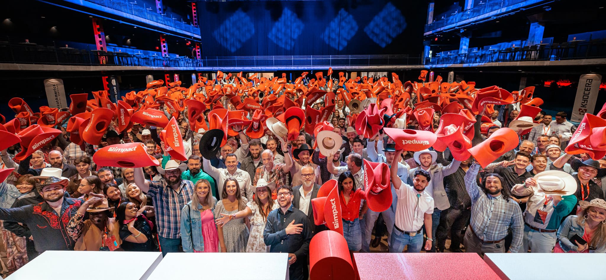 The Impact staff, a huge crowd, smiling and waving at the camera while holing up red foam cowboy hats