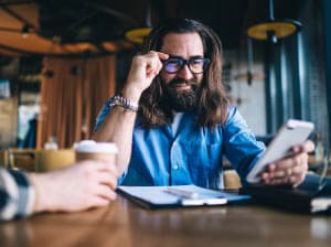 A man holding the corner of his glasses and looking at the screen of his smartphone