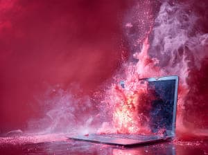 laptop exploding and on fire in front of red background