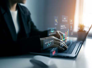 A person typing on a laptop with digital icons floating above the keyboard