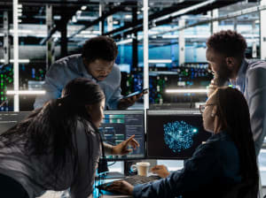 A group of four professionals grouped around a number of monitors