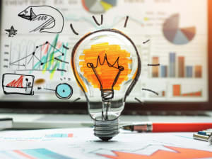 A hand drawn lightbulb on a crafting table with colorful charts behind