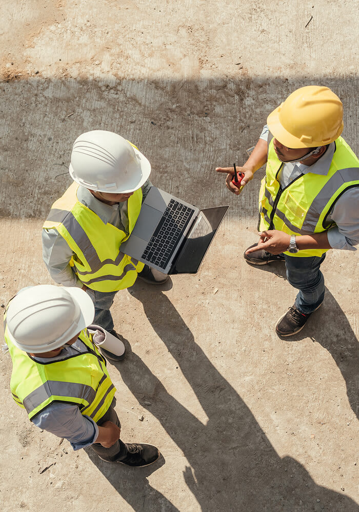 Three construction workers discuss priorities while one works on a laptop