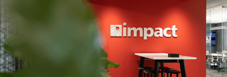 Common area with bar table and stools, Impact Networking logo on the red wall behind it | Impact Networking office in Riverside