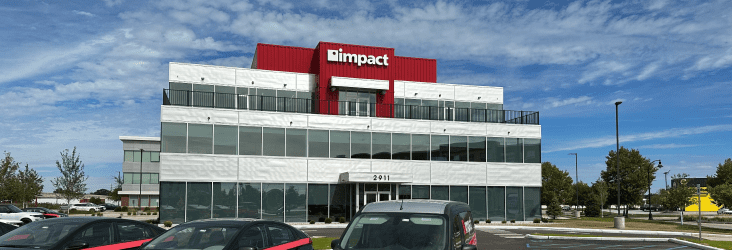 Black sedan with a red wrap around the headlights parked in front of a 3 story glass building with Impact logo at the top.